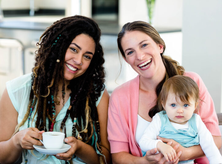 Portrait of two women smiling and sitting on sofa with a baby